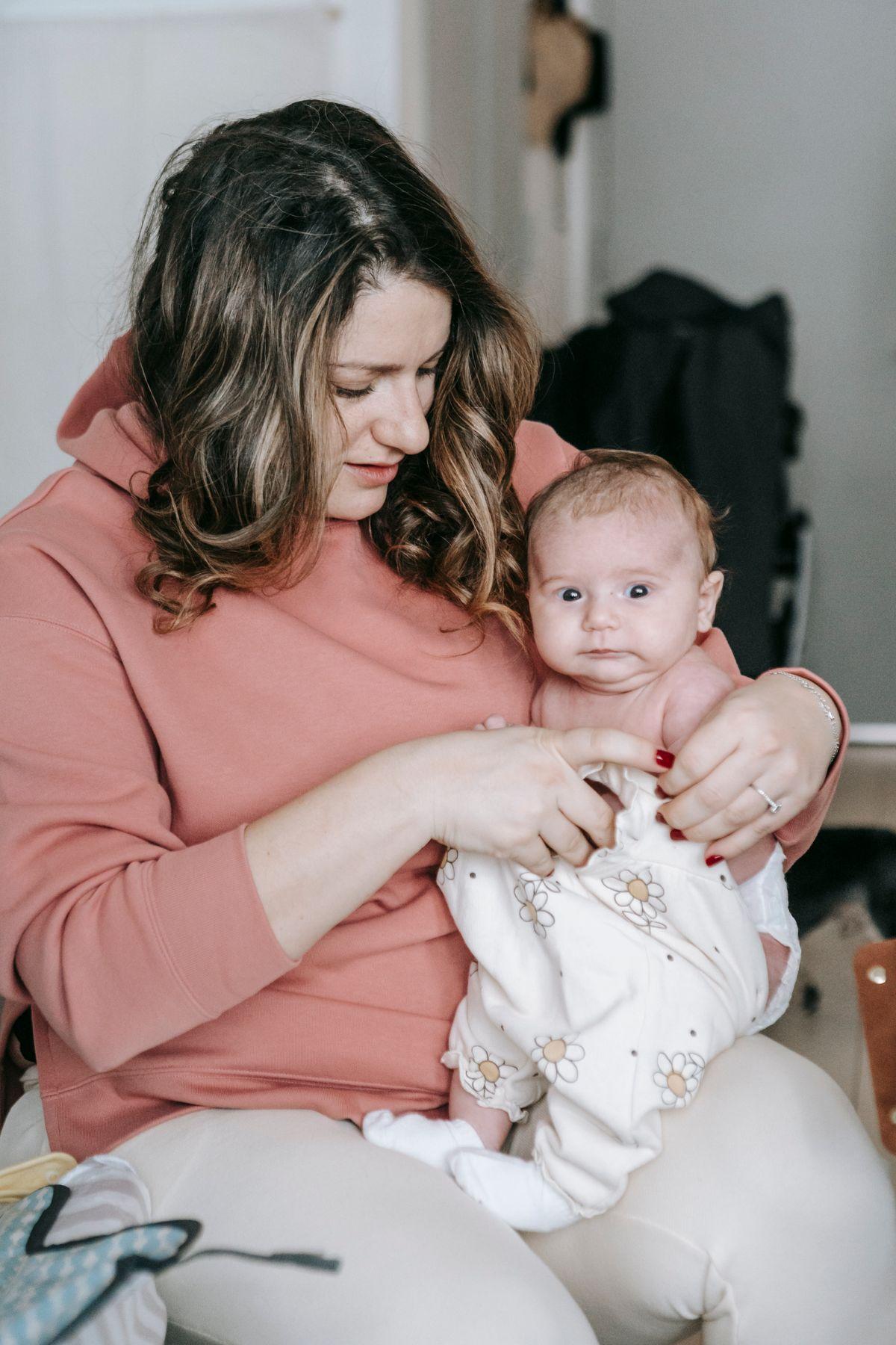 A caregiver gently dressing a bright-eyed baby during the day