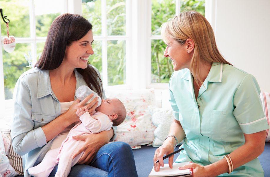 A caregiver coaching a mother while she bottle-feeds her baby at home
