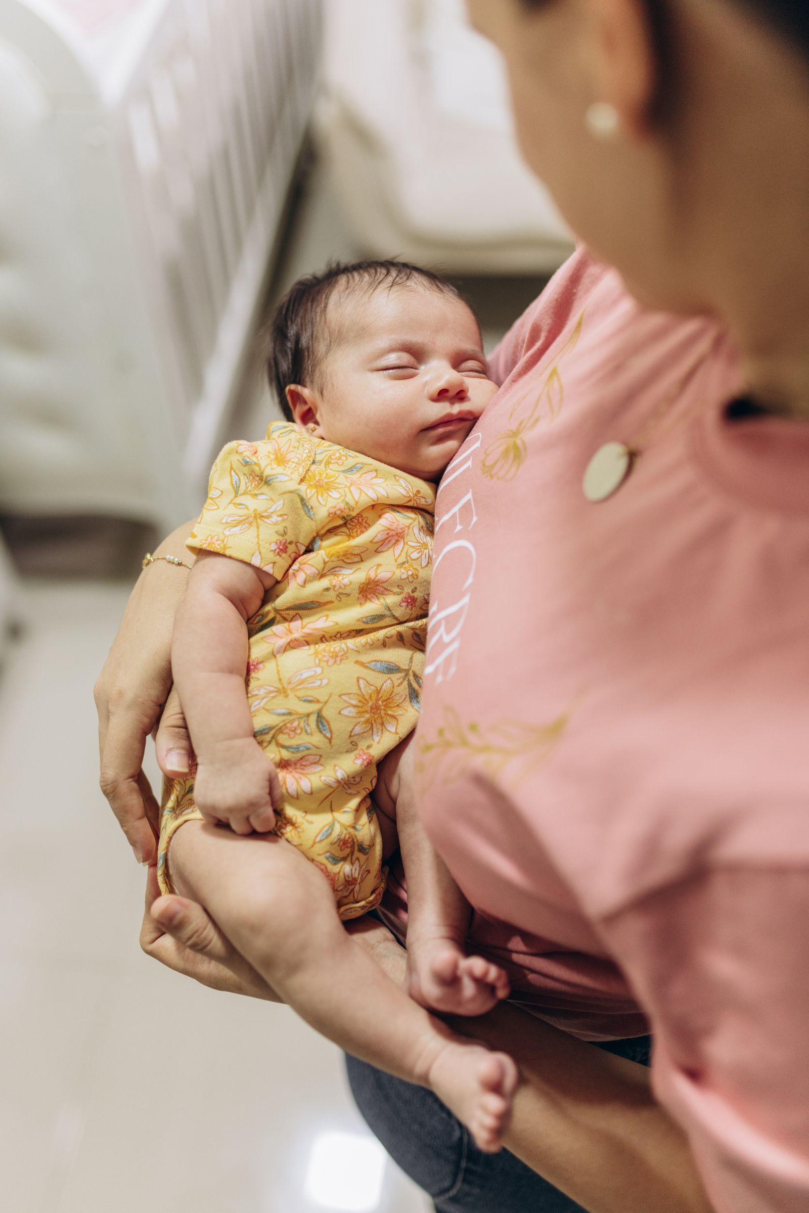 A mother settling her sleeping newborn beside the crib