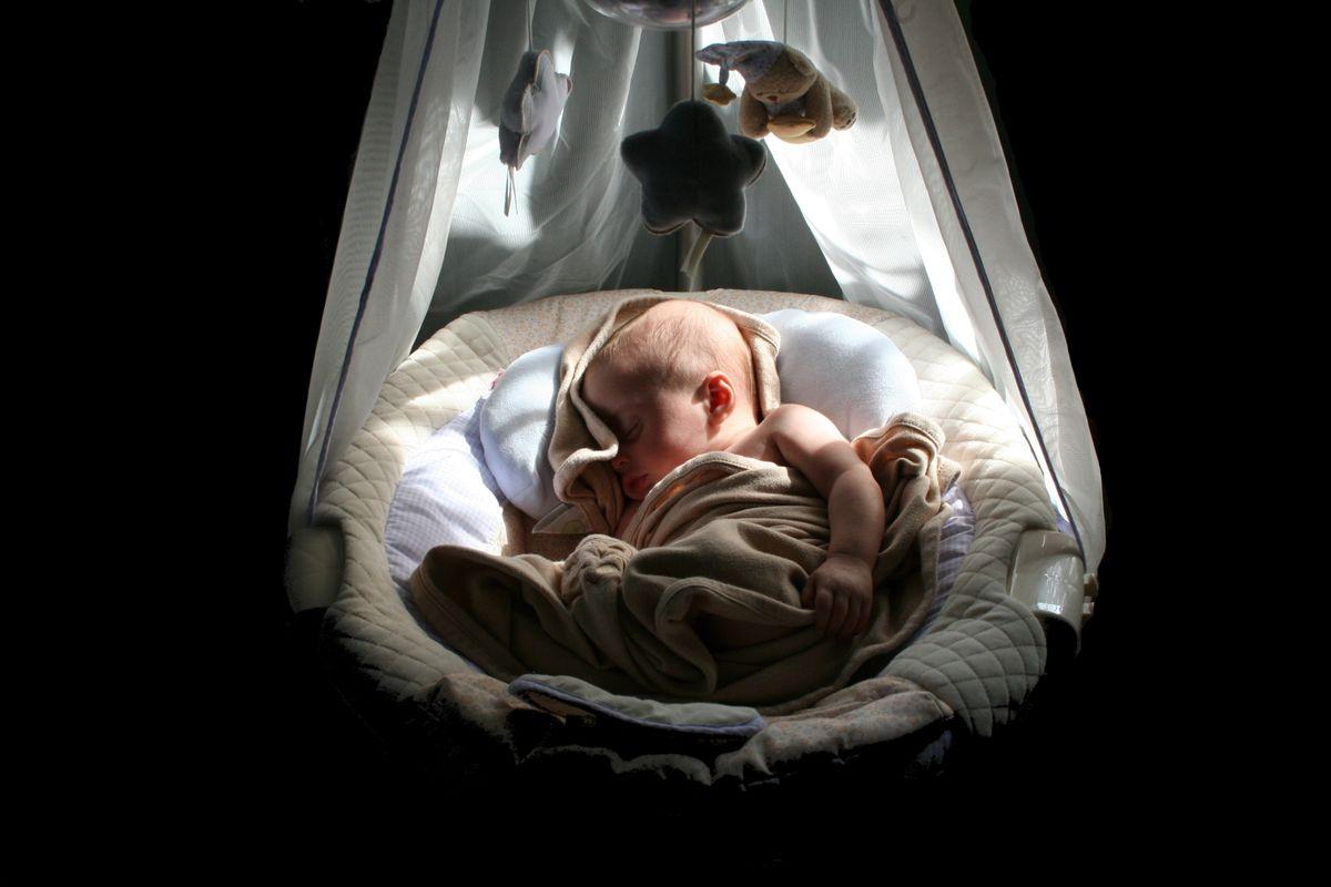A newborn sleeping peacefully in a bassinet beneath a mobile